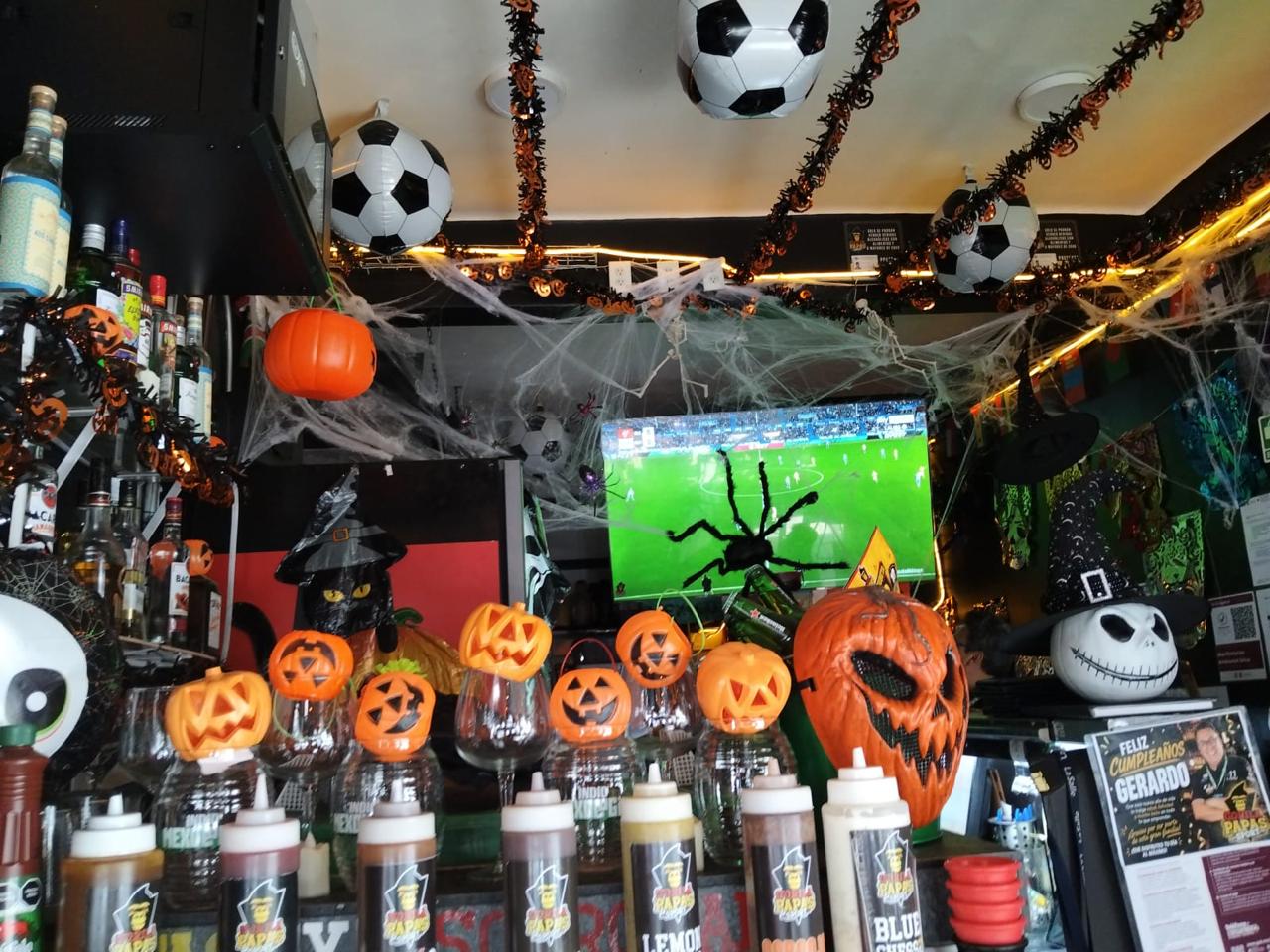 Televisores transmitiendo fútbol con araña gigante y copas de calabaza